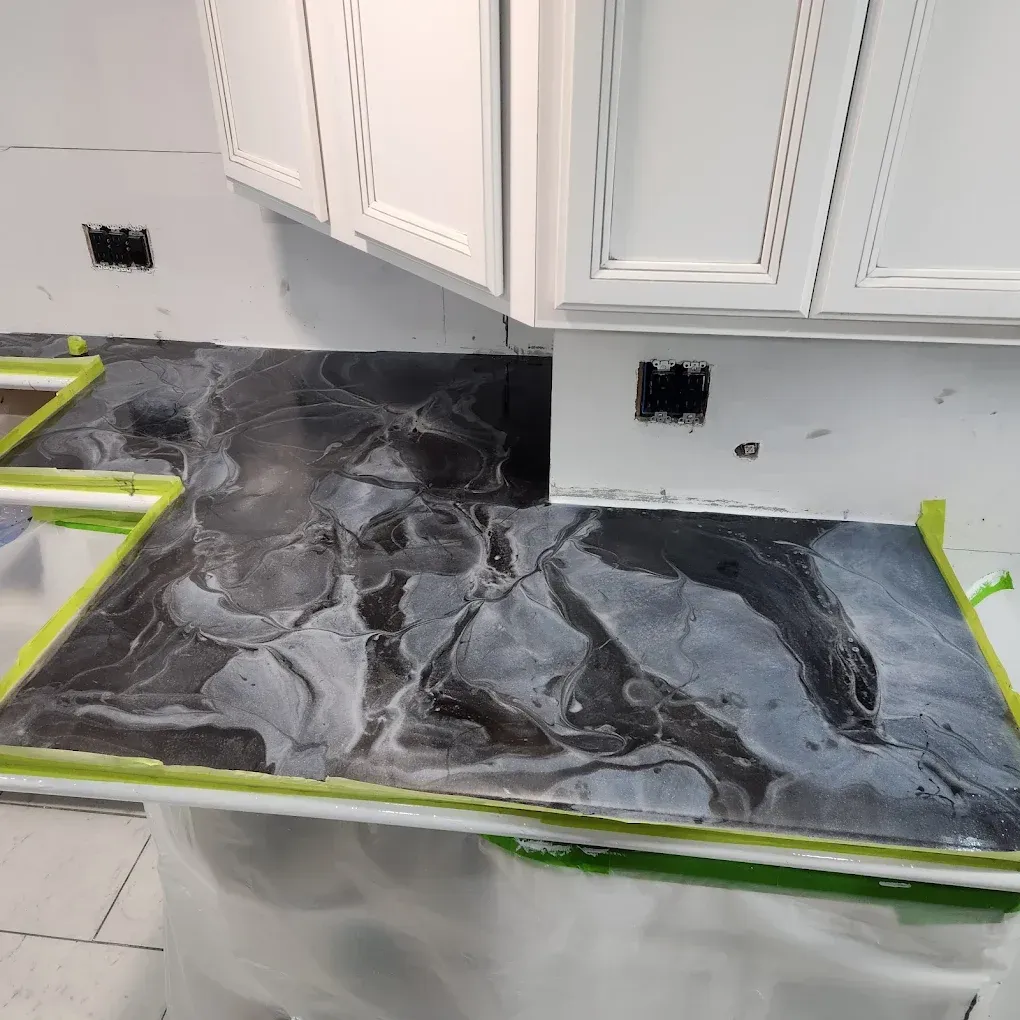 Kitchen countertop covered in gray-and-black marble contact paper, with white cabinets above and green painter’s tape edges