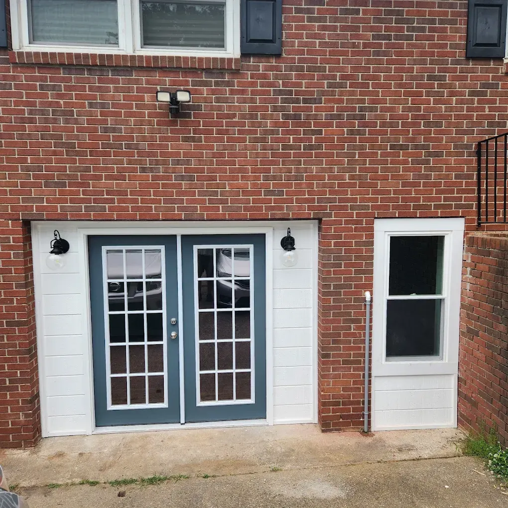 Brick townhouse basement entrance with blue double doors and a white side door.