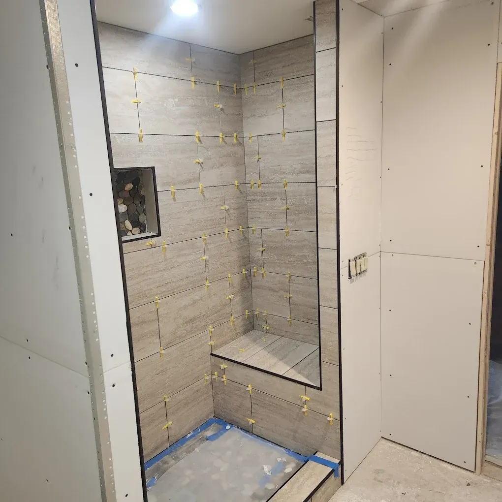 Unfinished shower alcove with tiled walls, built-in bench, and exposed drywall.