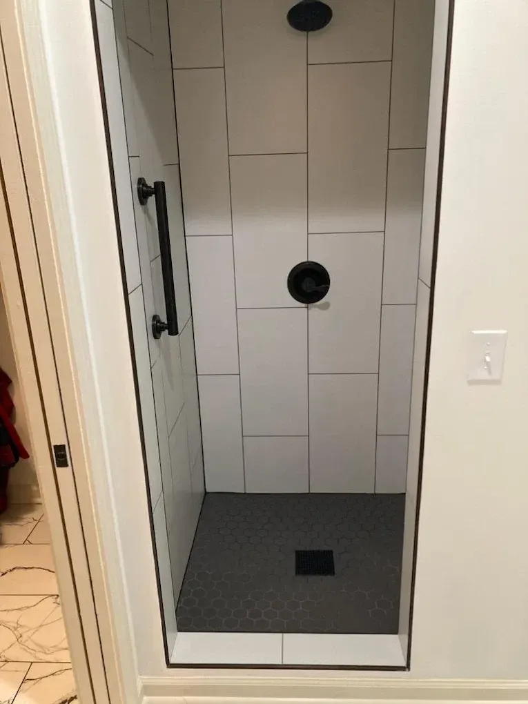 Small tiled shower stall with a gray pebble floor and two black fixtures inside a bathroom.