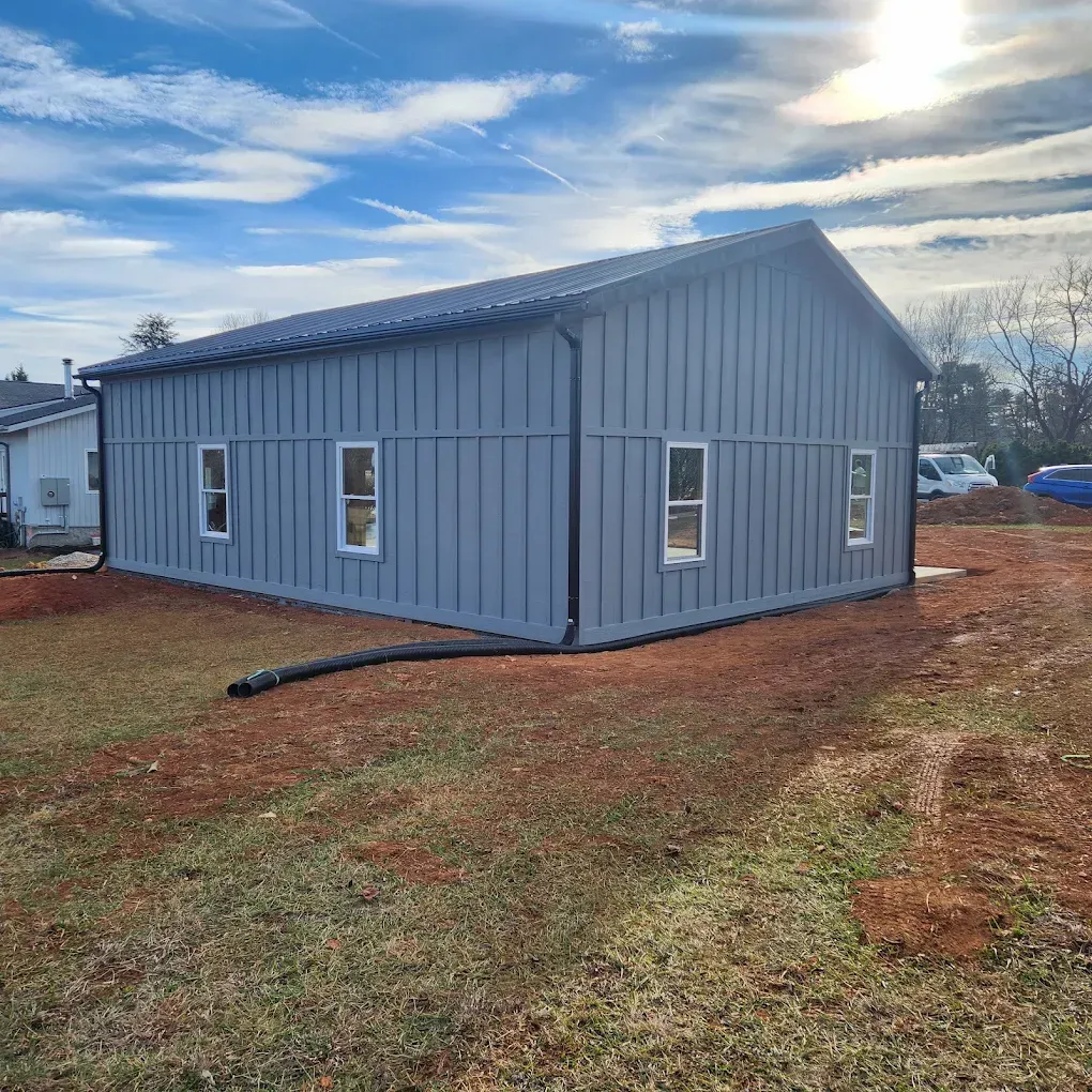 Gray metal building with white-trim windows on a dirt lot under a cloudy sky