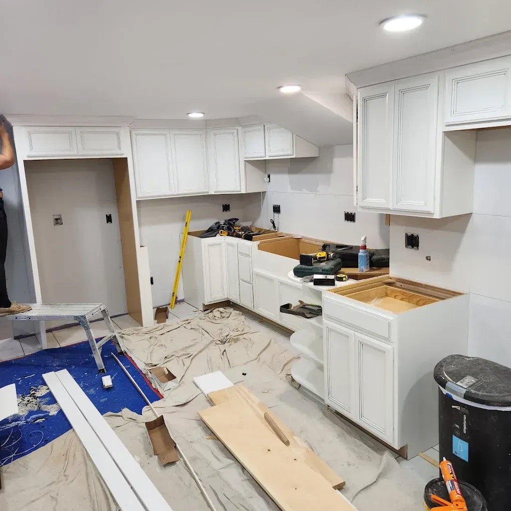 Kitchen under renovation with white cabinets, tools, drop cloths, and debris on the floor