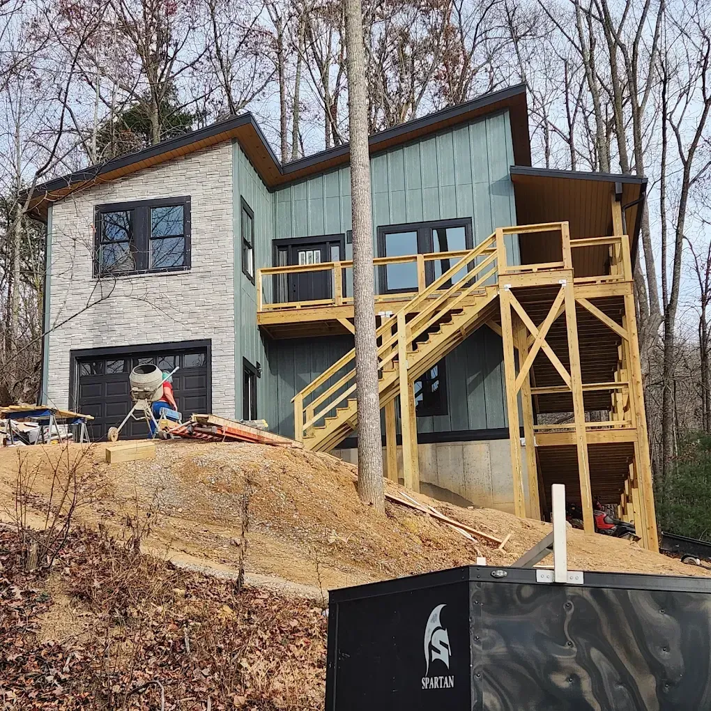 New house under construction on a wooded hillside with workers and wooden deck stairs