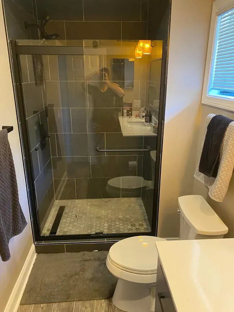 Bathroom with glass shower, vanity, toilet, and towels on dark walls and white tile។
