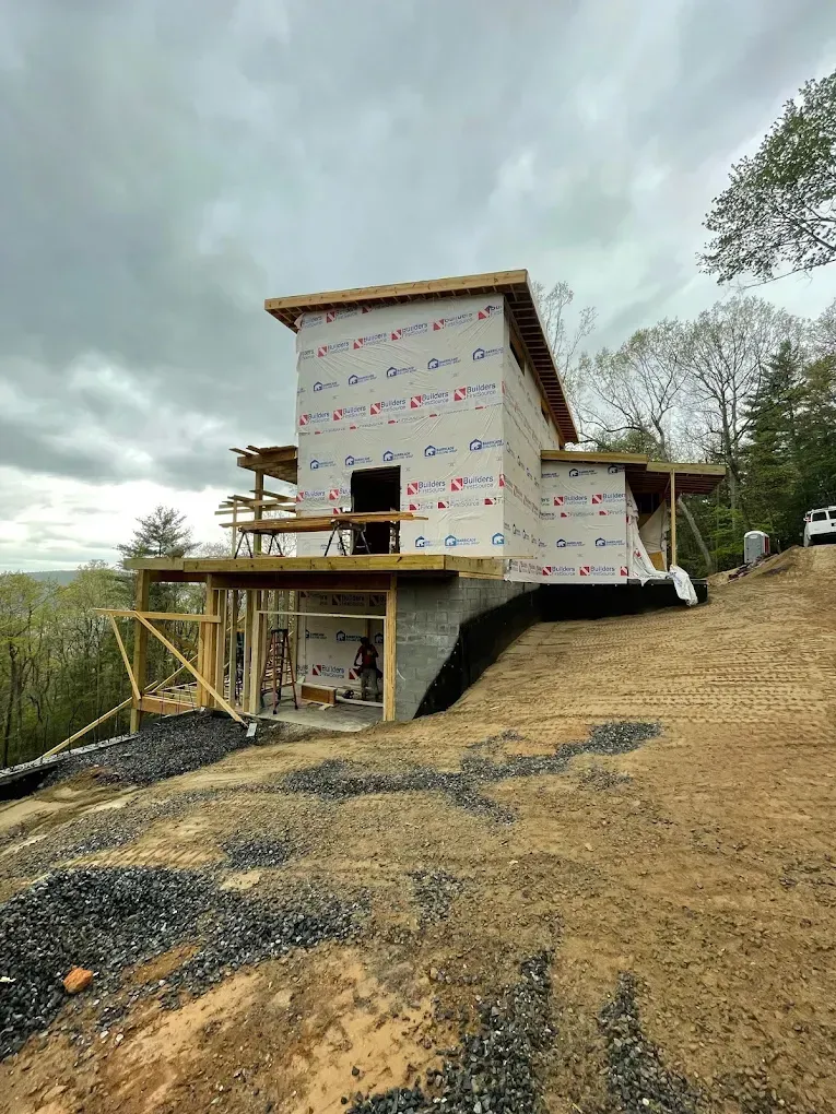 Partially built house wrapped in white house wrap on a gravel lot under a cloudy sky