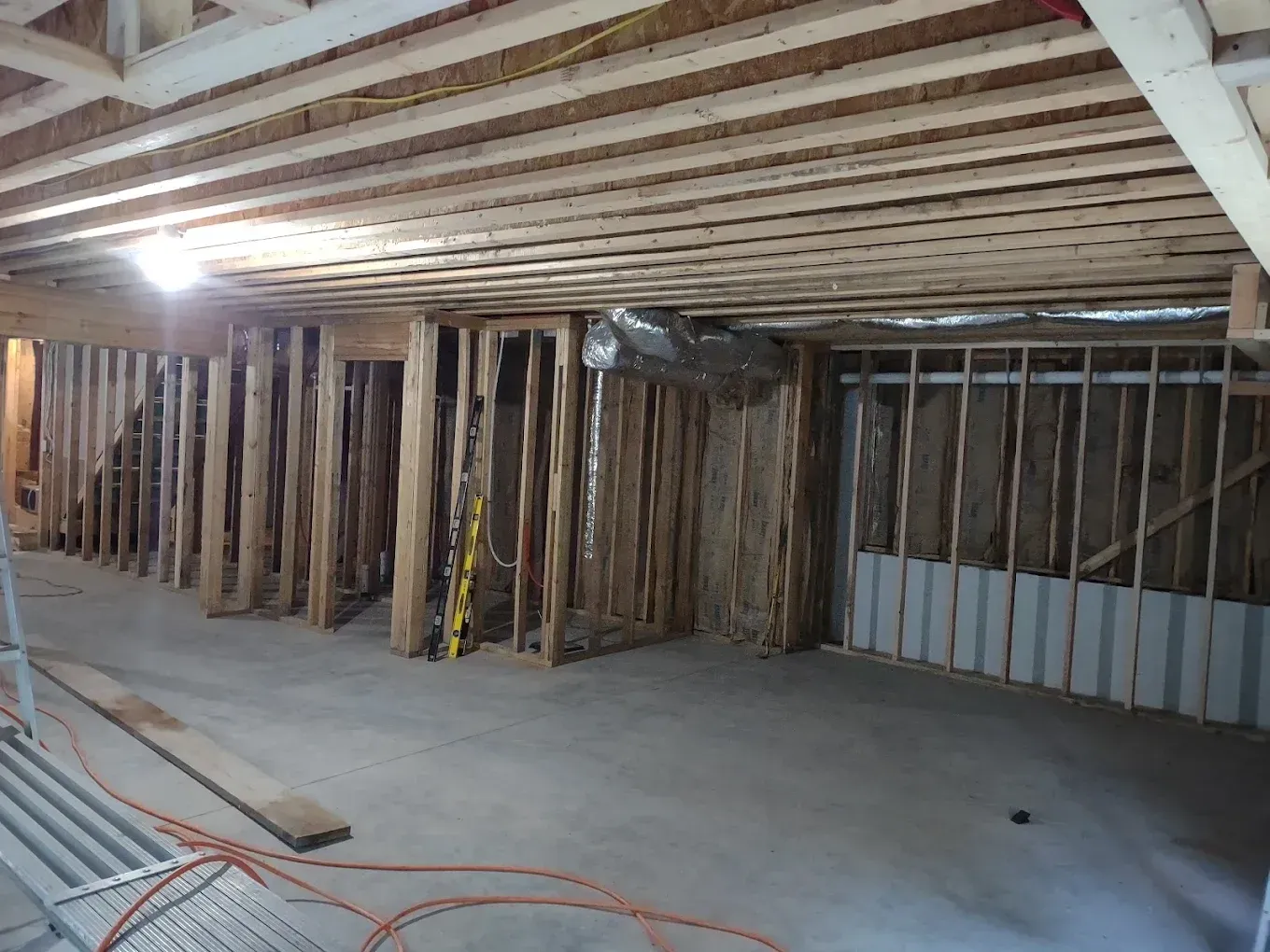 Unfinished basement with exposed wooden framing, concrete floor, and construction materials on the ground.