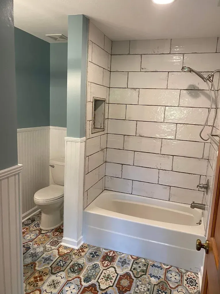 Bathroom with white subway-tile shower, toilet alcove, and patterned floor tiles