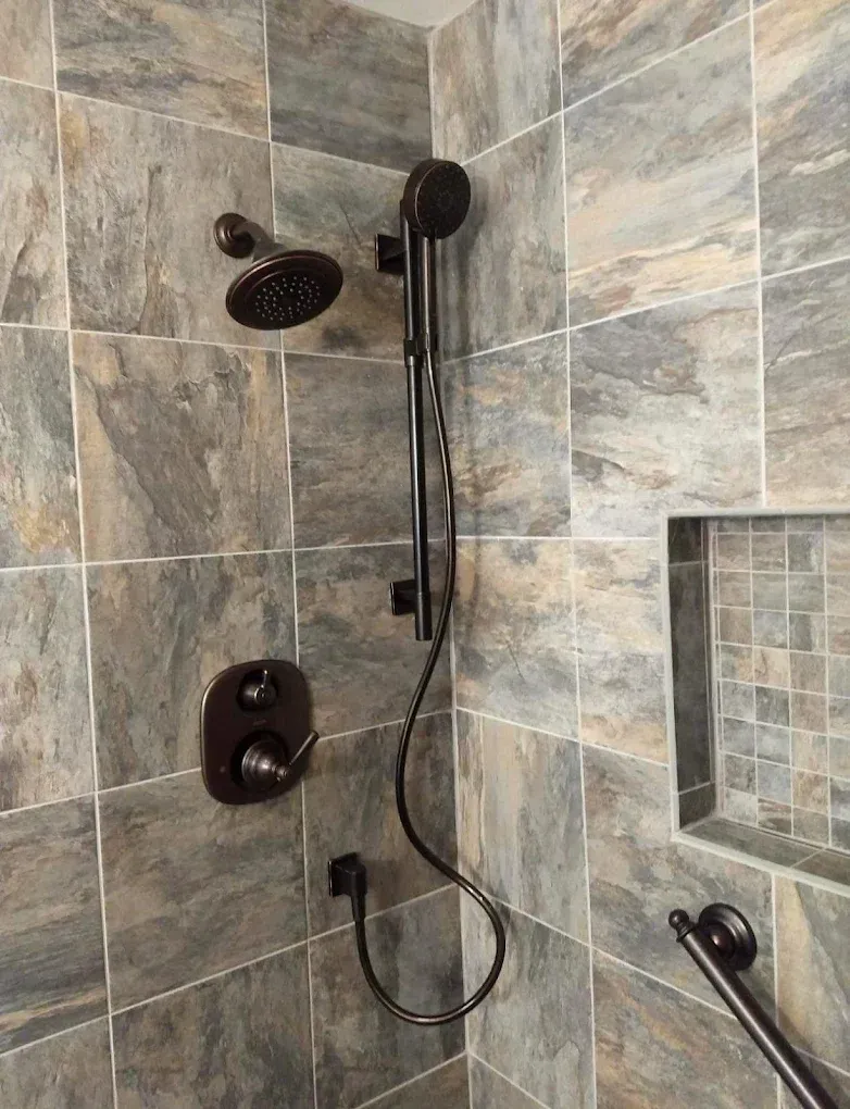 Stone-tile shower with wall-mounted handheld showerhead and built-in shelf nook.
