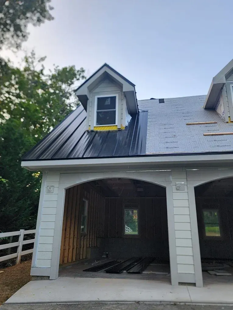 Front of a house under construction with a black roof, white siding, and an open garage.
