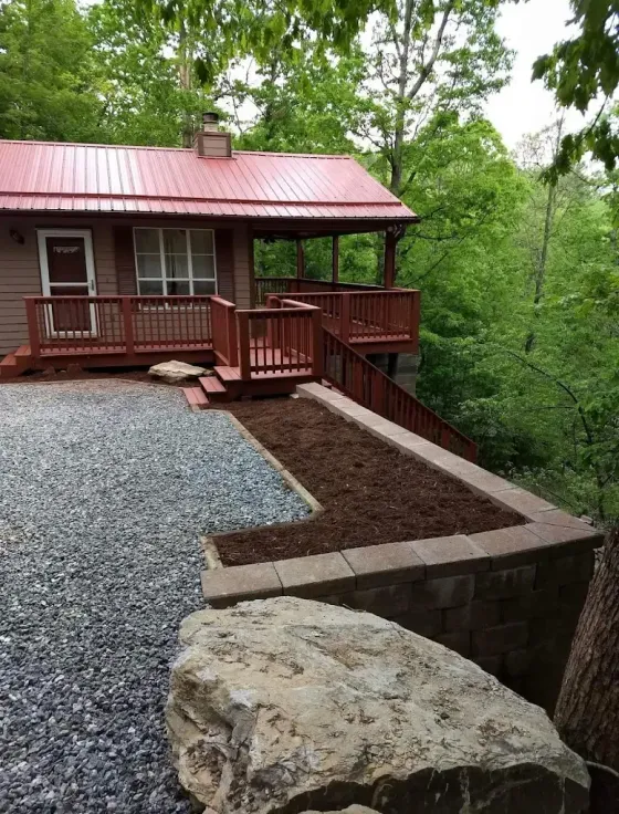 Red cabin with a gravel yard and wooden deck on a wooded hillside