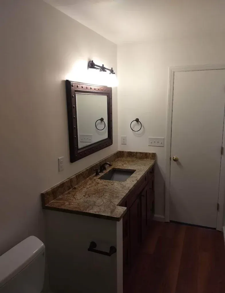 Bathroom with granite vanity, wall mirror, light fixture, toilet, and closed white door