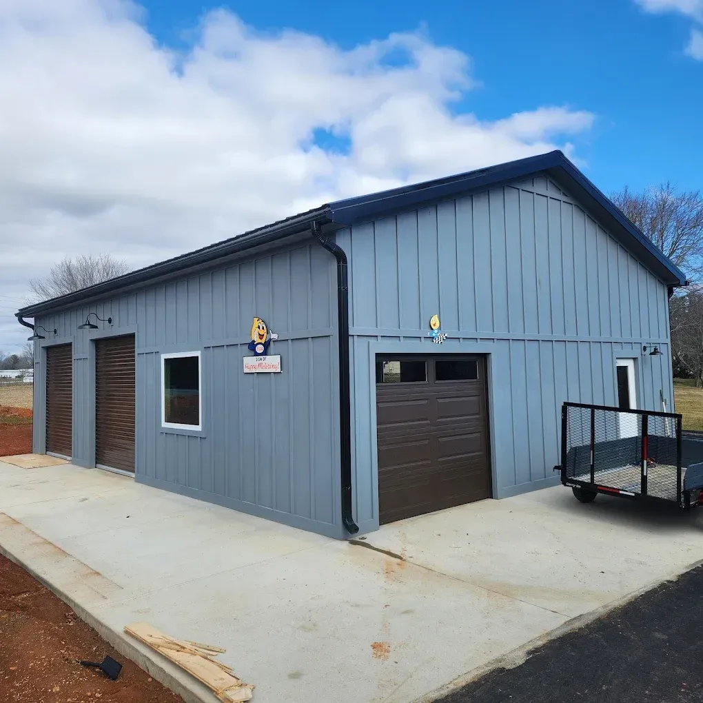Blue metal garage building with brown doors on a concrete pad under a cloudy sky