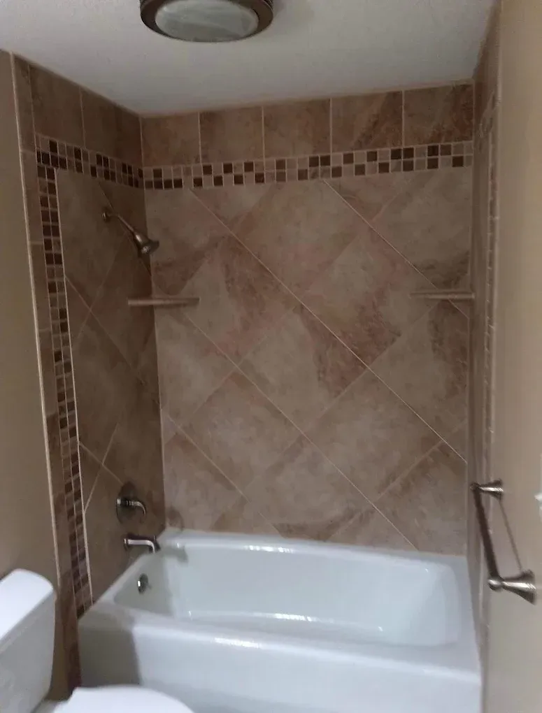 Small tiled bathroom with a white bathtub, showerhead, and beige decorative wall tiles.