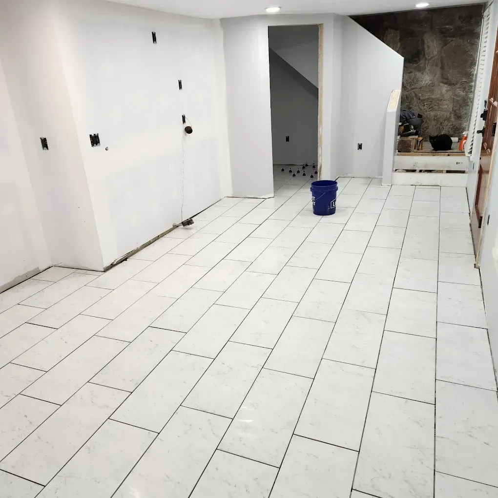 Empty white-tiled room under renovation with a blue bucket near the center.