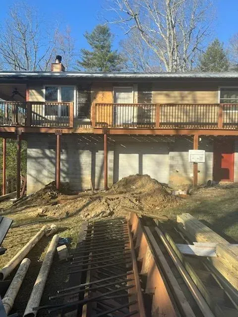 Two-story house with deck and bare trees; construction materials and trench in the foreground