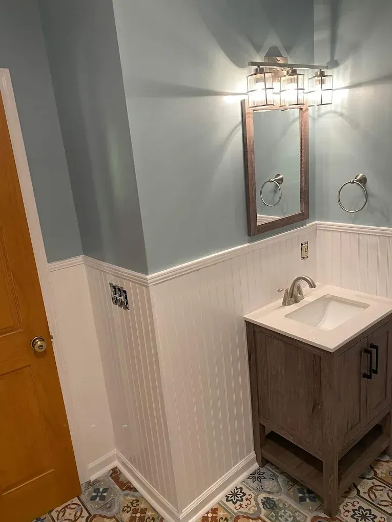Small bathroom vanity with mirror, wall light, gray walls, white wainscoting, and tiled floor.