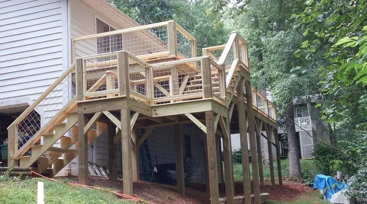 Wooden deck and stairs under construction beside a house in a wooded yard