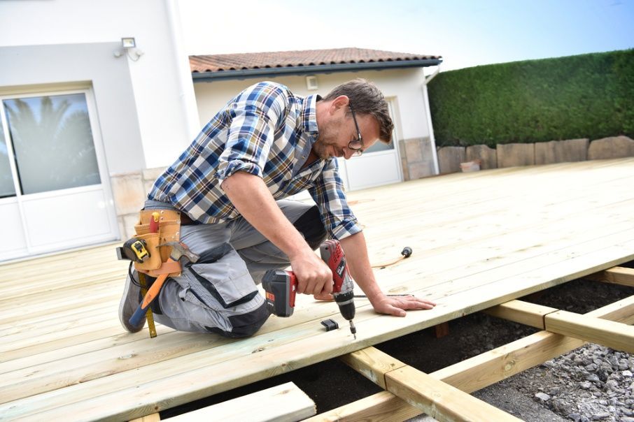 A Man is Kneeling Down Using a Drill on a Wooden Deck — Mick's Carpentry & Maintenance In Machans Beach, QLD