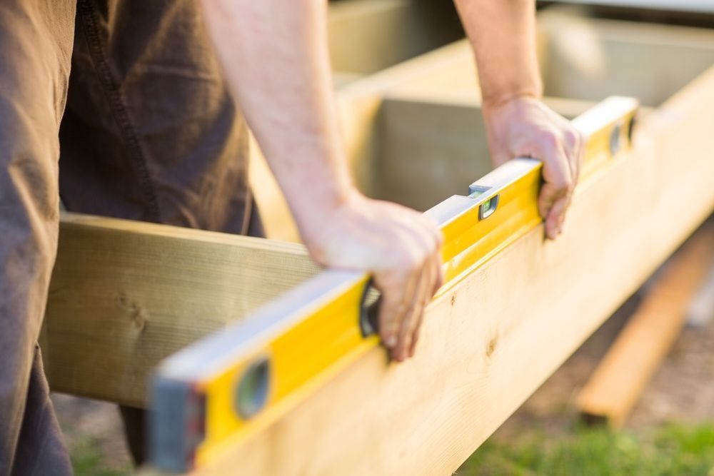A Person is Holding a Level Over a Piece of Wood — Mick's Carpentry & Maintenance In Machans Beach, QLD