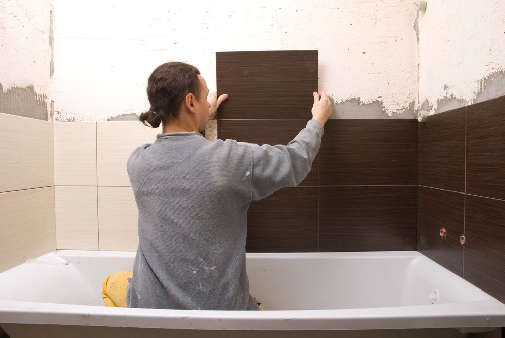 A Man is Sitting in a Bathtub While Installing Tiles on the Wall — Mick's Carpentry & Maintenance In Machans Beach, QLD