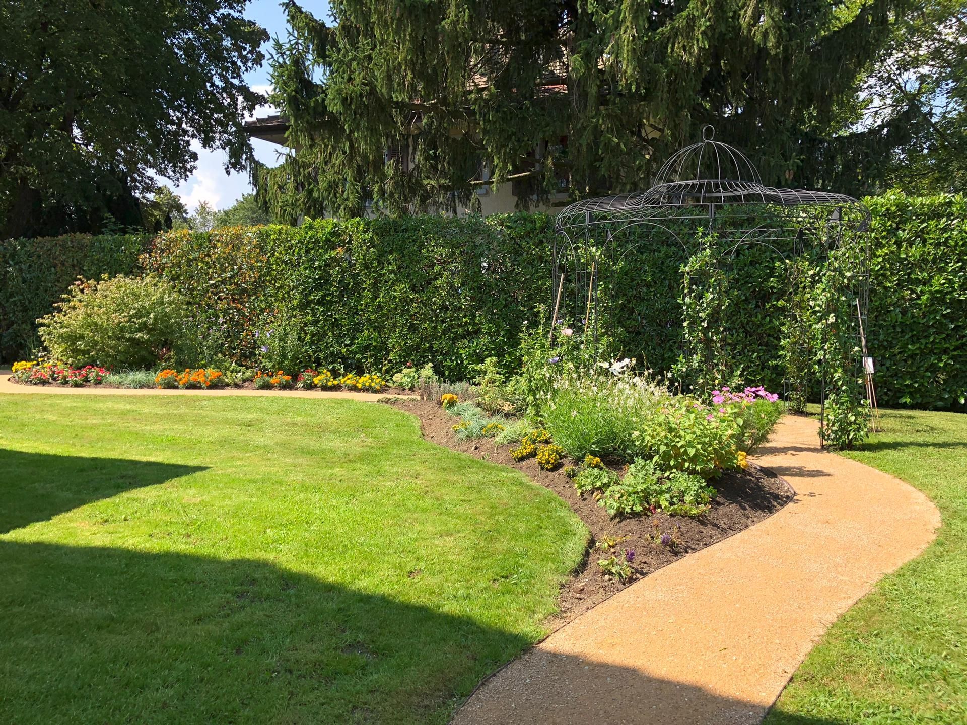 un chemin serpente à travers un jardin verdoyant avec un gazebo en arrière-plan .