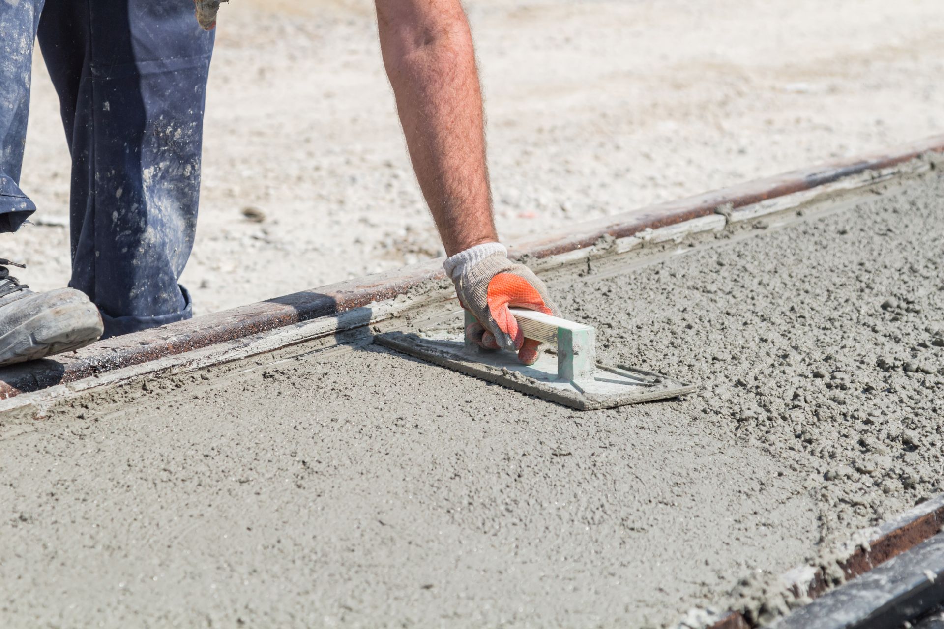 Worker smoothing wet concrete with a hand trowel on a sidewalk