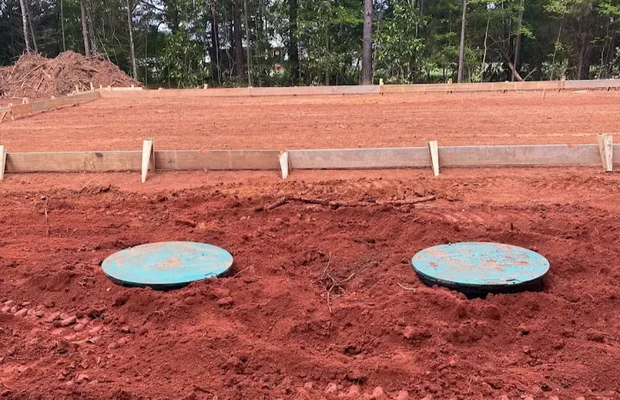Two green circular covers in red dirt near a construction site foundation.