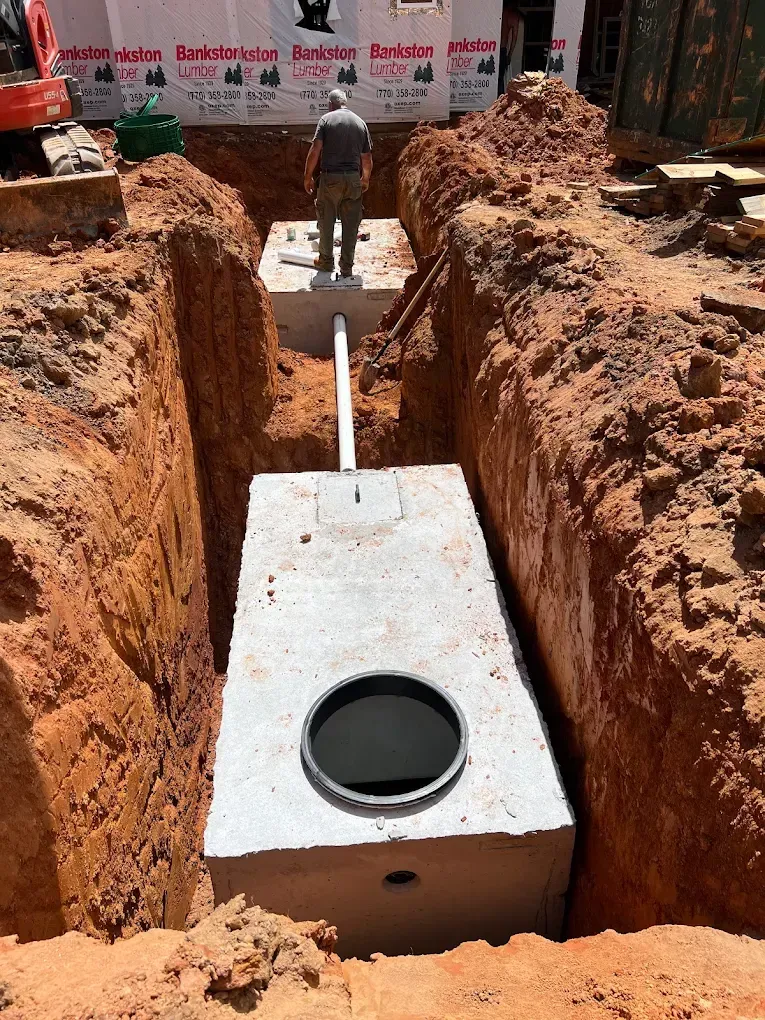 Concrete septic tank in a trench at a construction site; a person stands nearby.