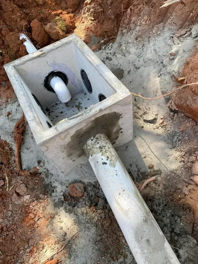 Concrete box with PVC pipes in an earthen setting; likely a septic system component during installation.