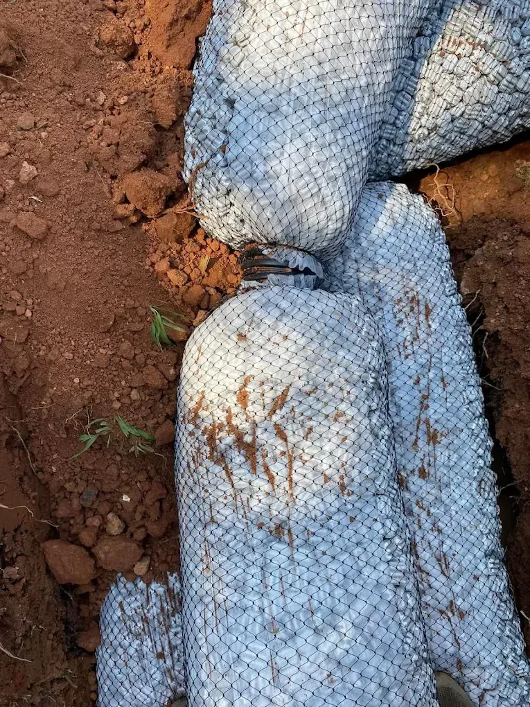 White mesh-wrapped structures, possibly for erosion control, in a brown dirt trench.