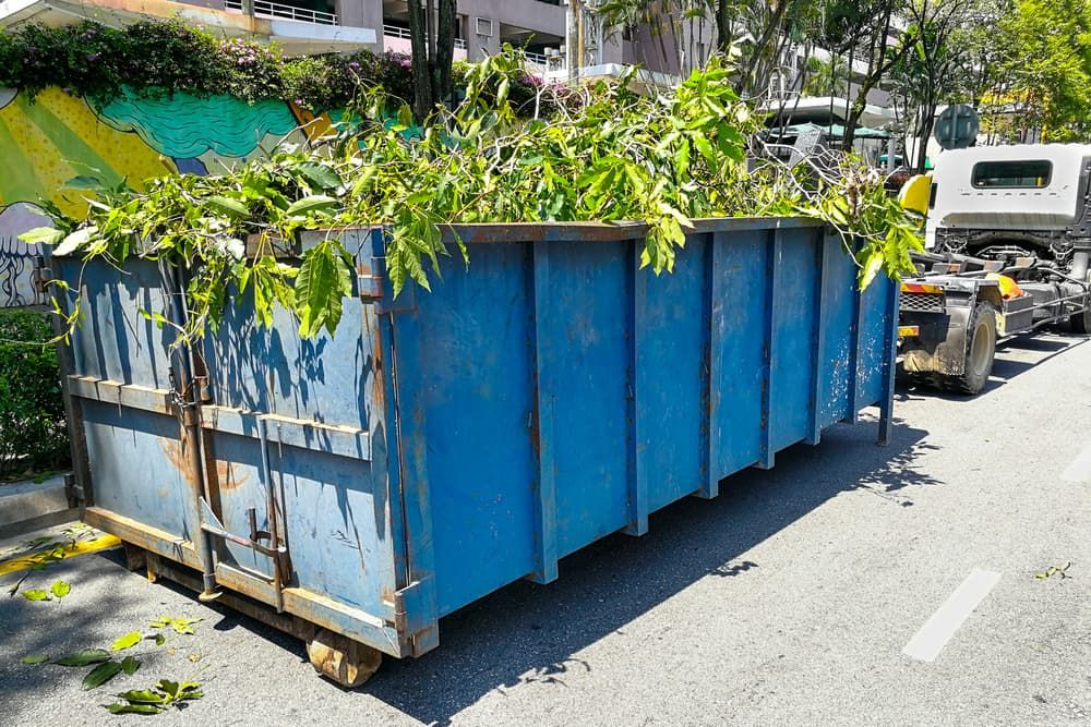 A Blue Dumpster Filled With Leaves is Parked on the Side of the Road — Ability Tree Service in Wingham, NSW