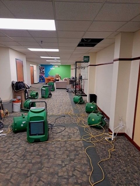 Hallway with green floor fans, extension cords, and ceiling tiles being repaired