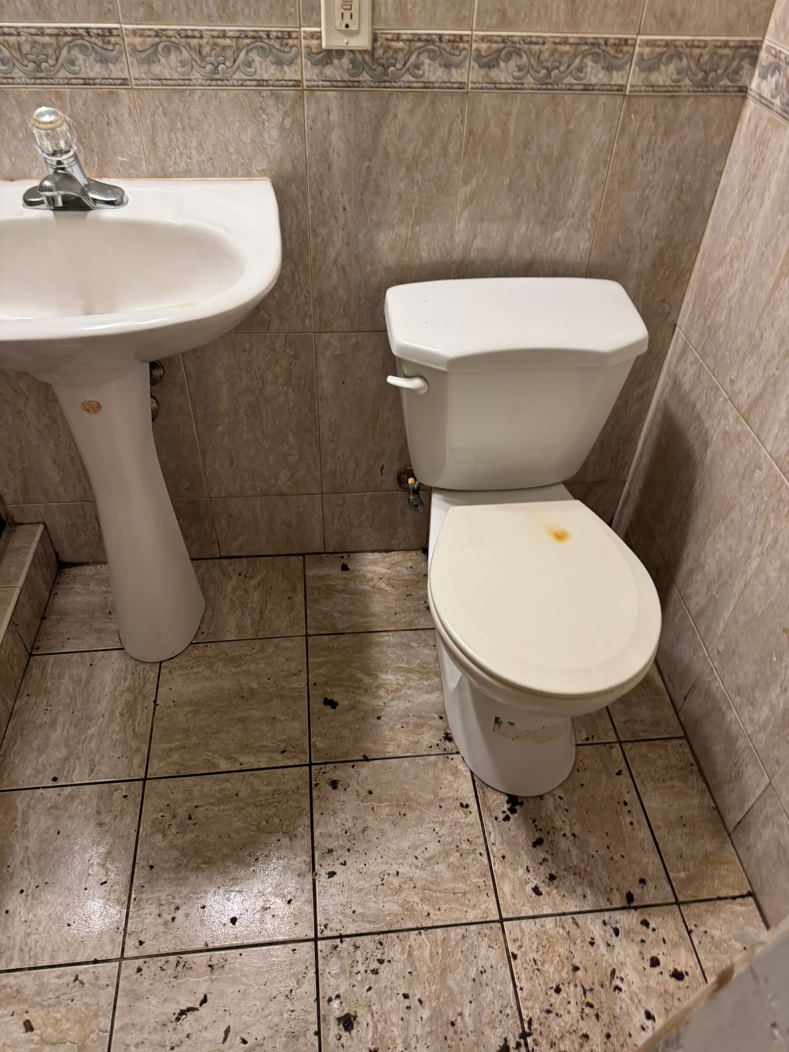 Small restroom with a white sink and toilet beside beige tiled walls and floor.