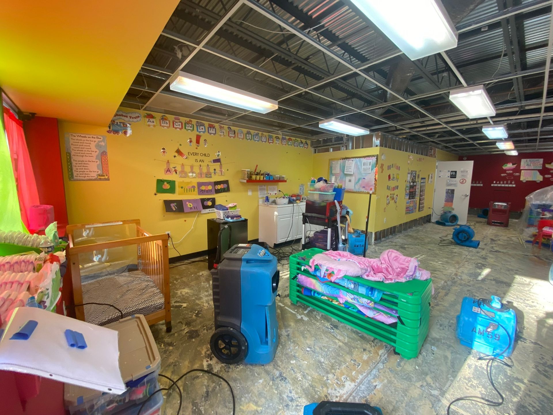 Bright cluttered workshop with yellow walls, tools, and stacked supplies on the floor.