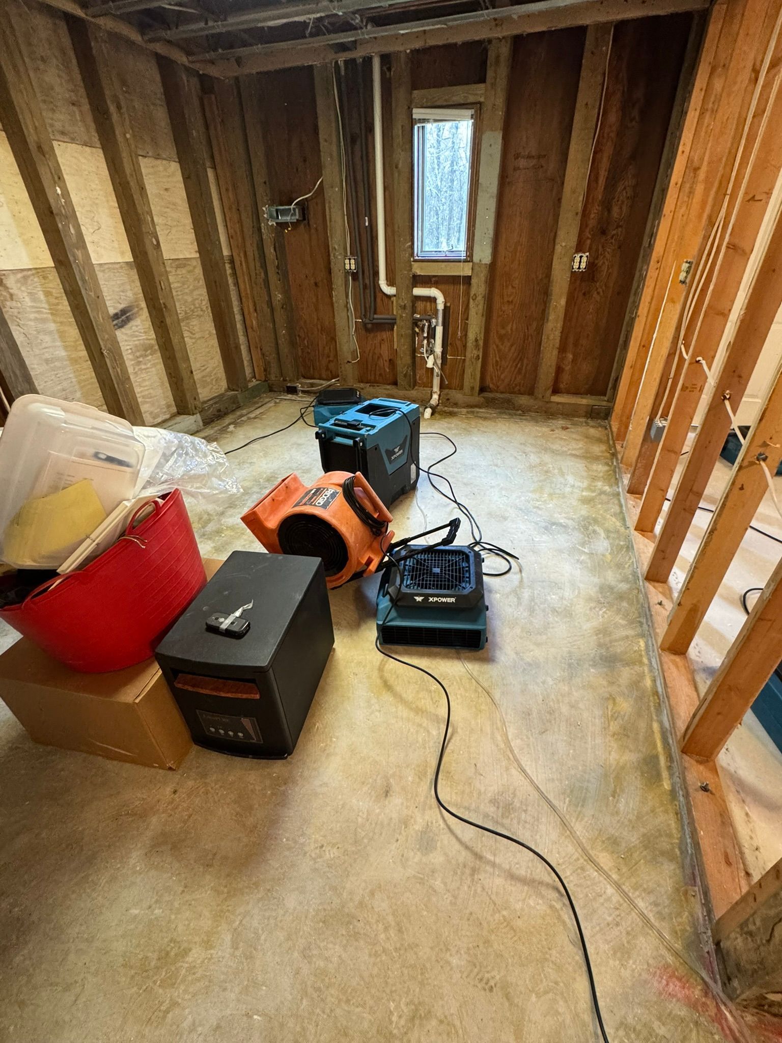 Unfinished room with exposed studs, tools, and materials on the floor near a small window.