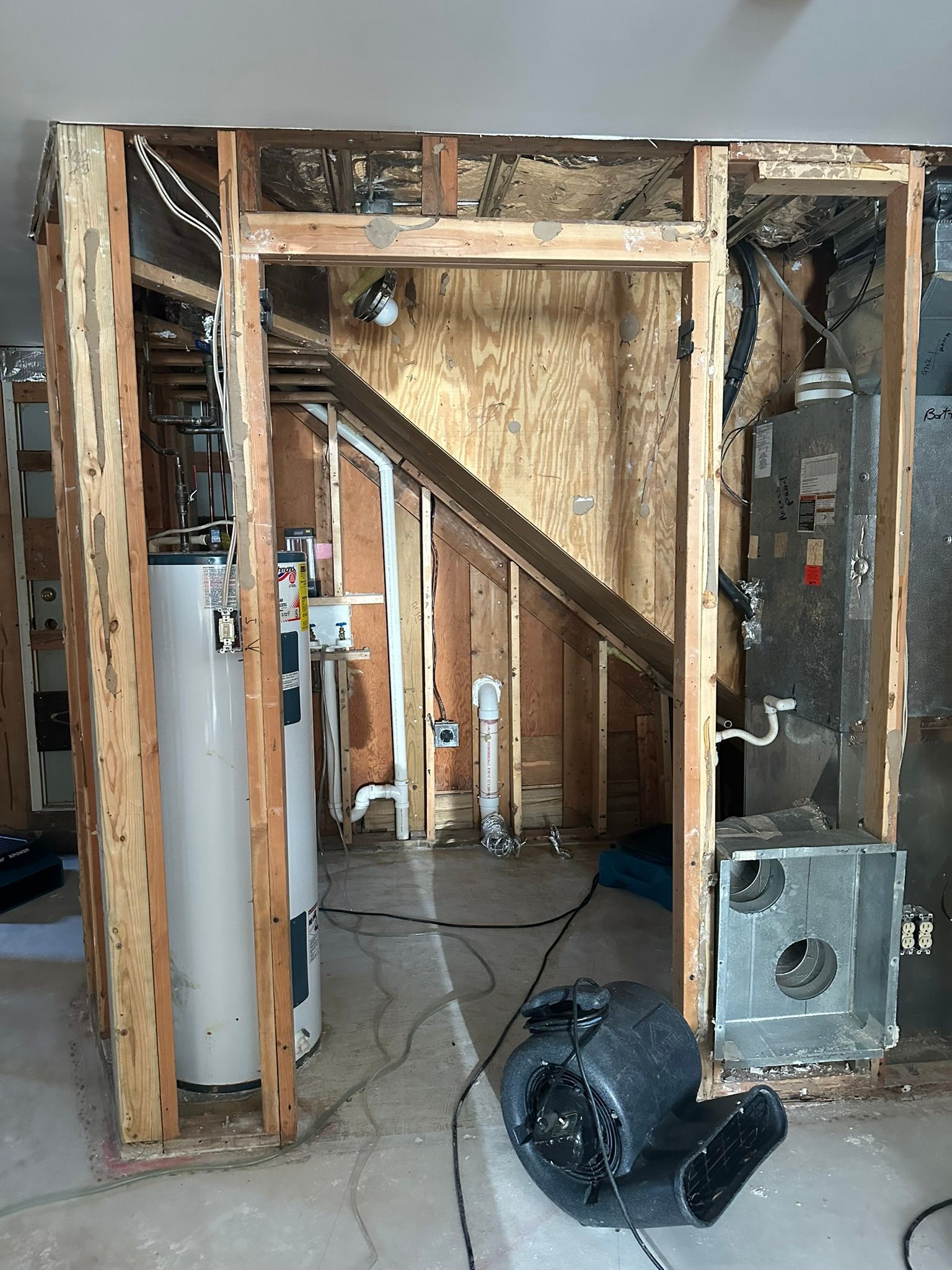Exposed wall framing and stairs in a gutted room, with a white water heater and debris on the floor
