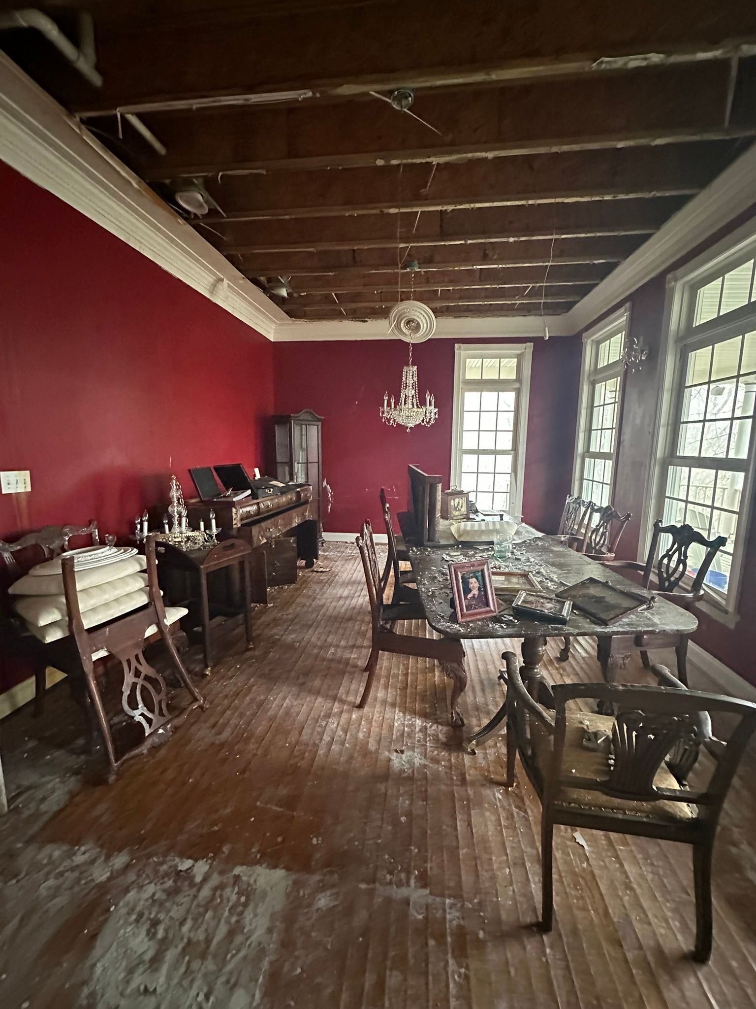 Red-walled dining room with wooden ceiling, glass table, chairs, and sunlight through windows.