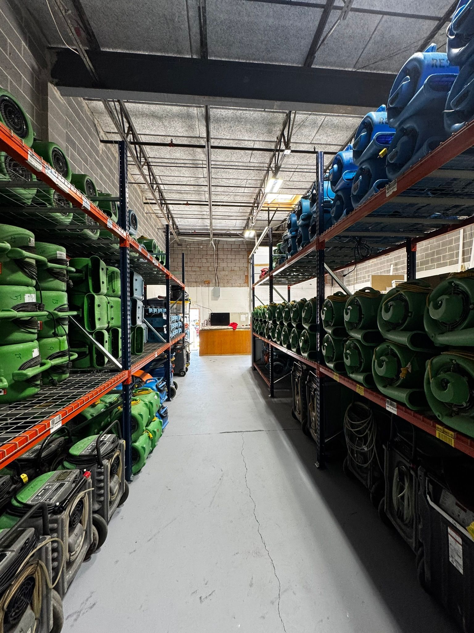 Aisle in a warehouse stocked with green and blue equipment on metal shelves.
