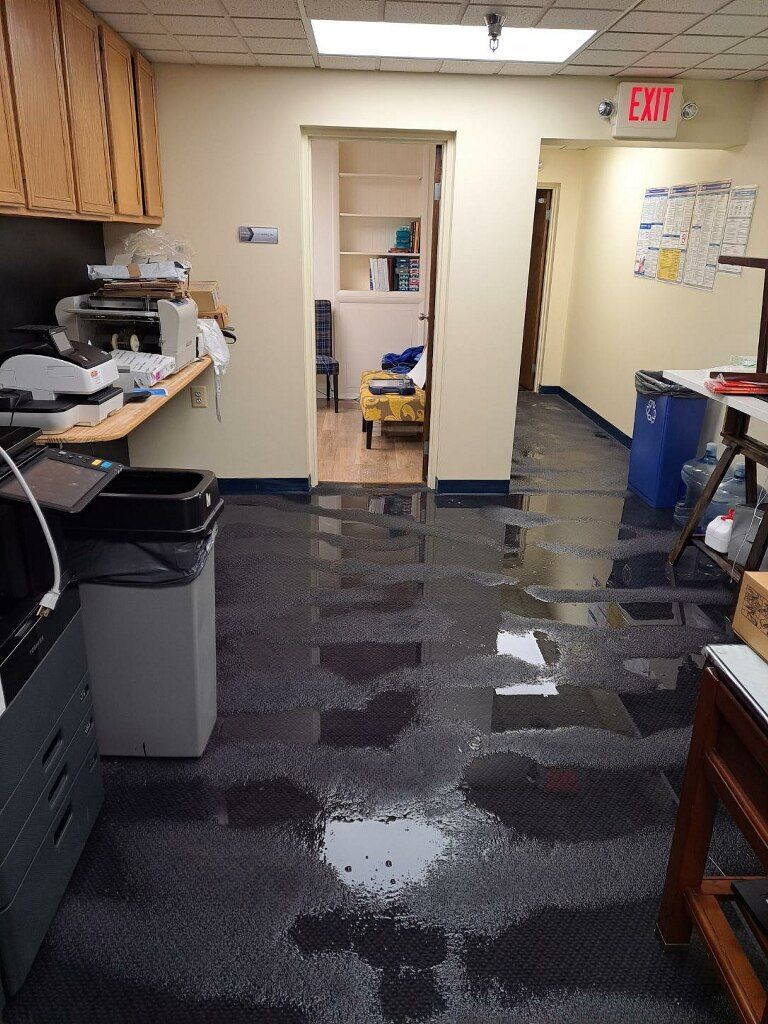 Office hallway with wet carpet, open doorway, trash bin, and EXIT sign