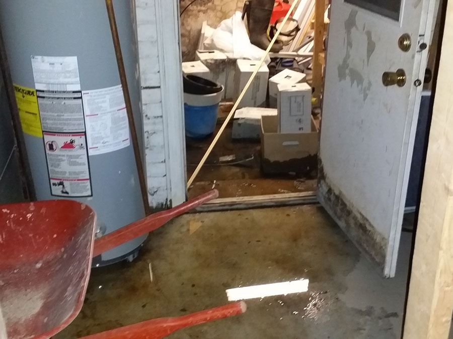 Messy basement entryway with a water heater, open door, and tools scattered on a wet floor.