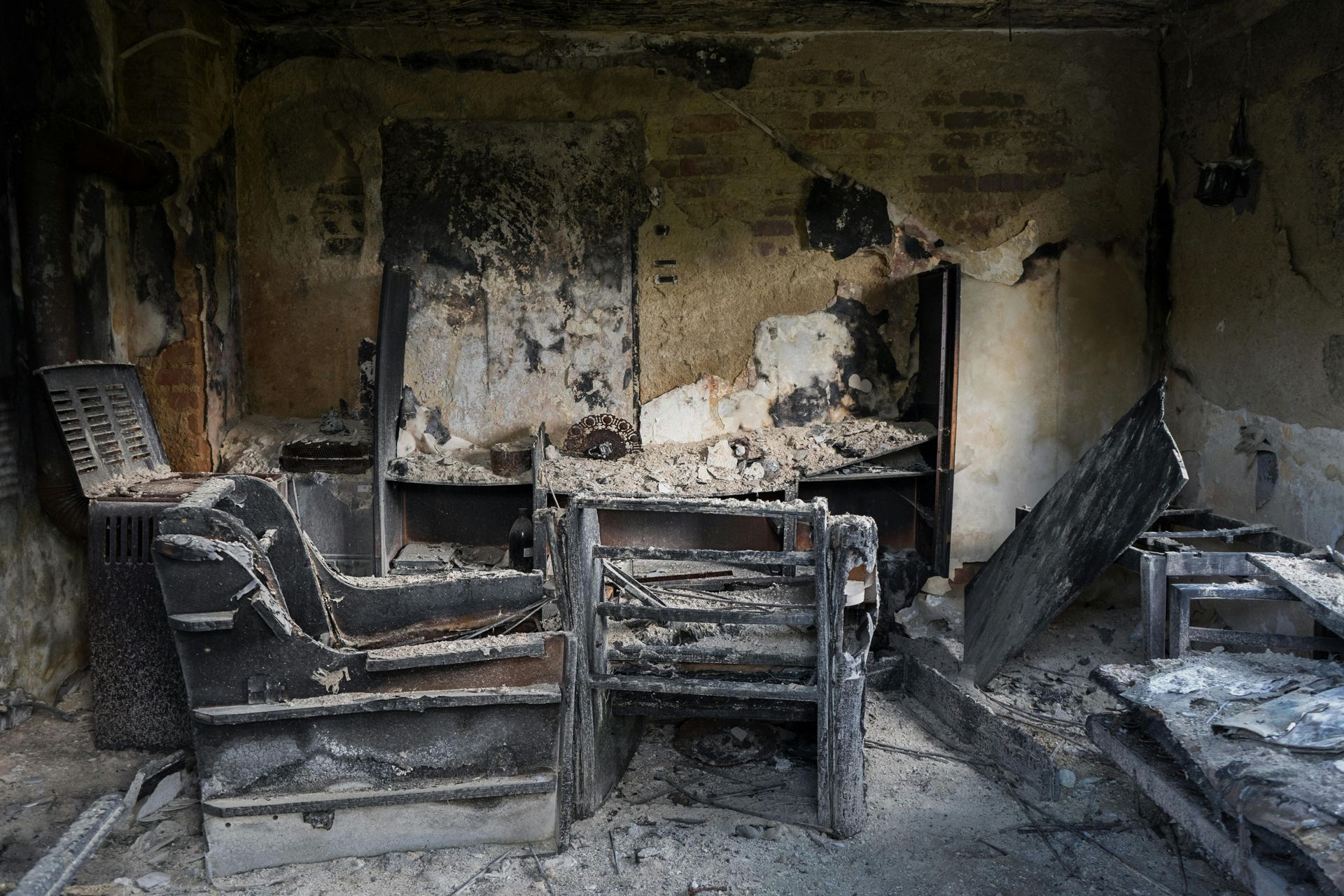 Burned room with charred furniture, blackened walls, and debris scattered across the floor