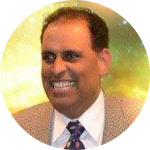 Smiling man in a tan suit, white shirt, and patterned tie against a yellow-green background