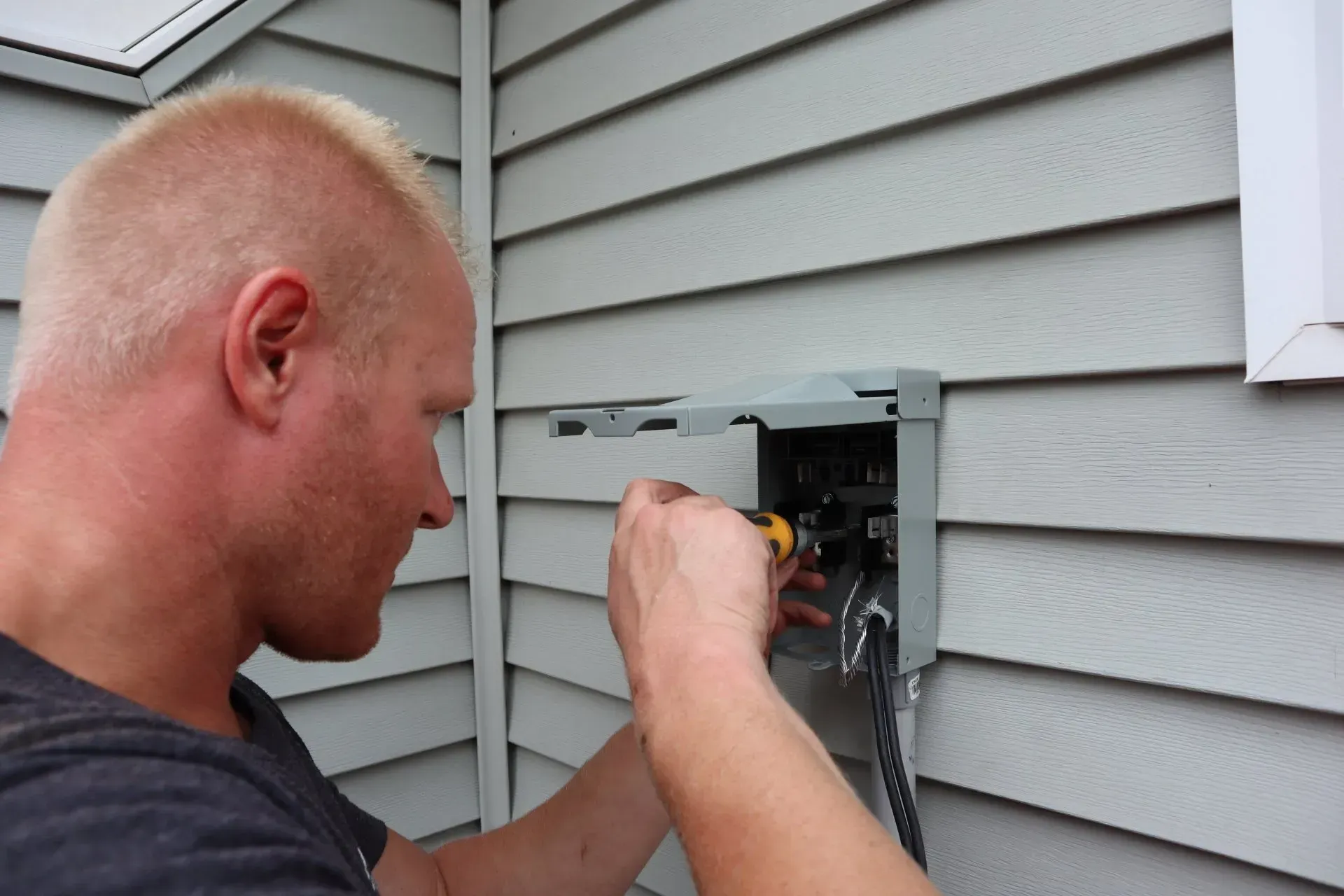A man is working on an electrical box on the side of a house.