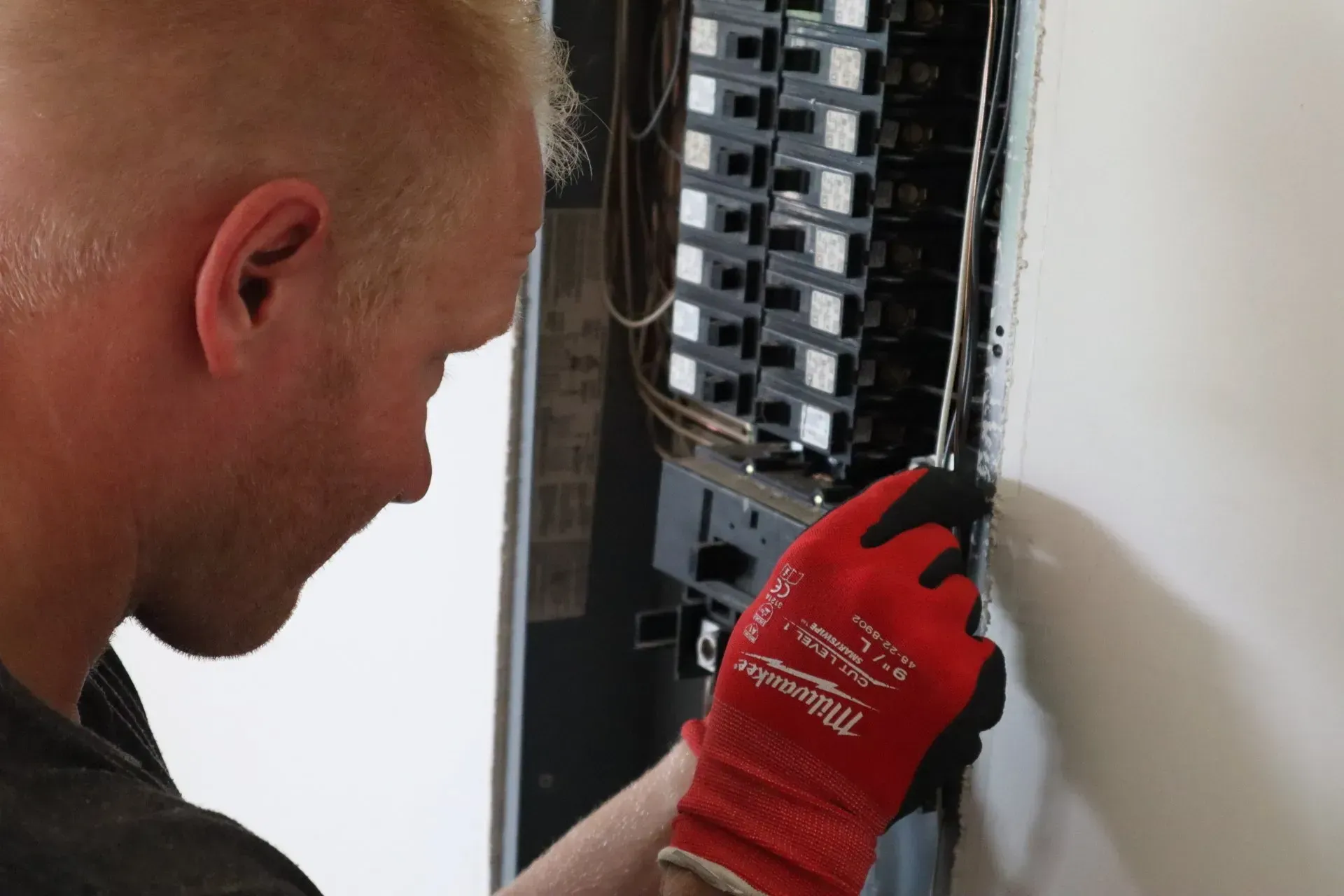 A man wearing red gloves is working on an electrical panel.
