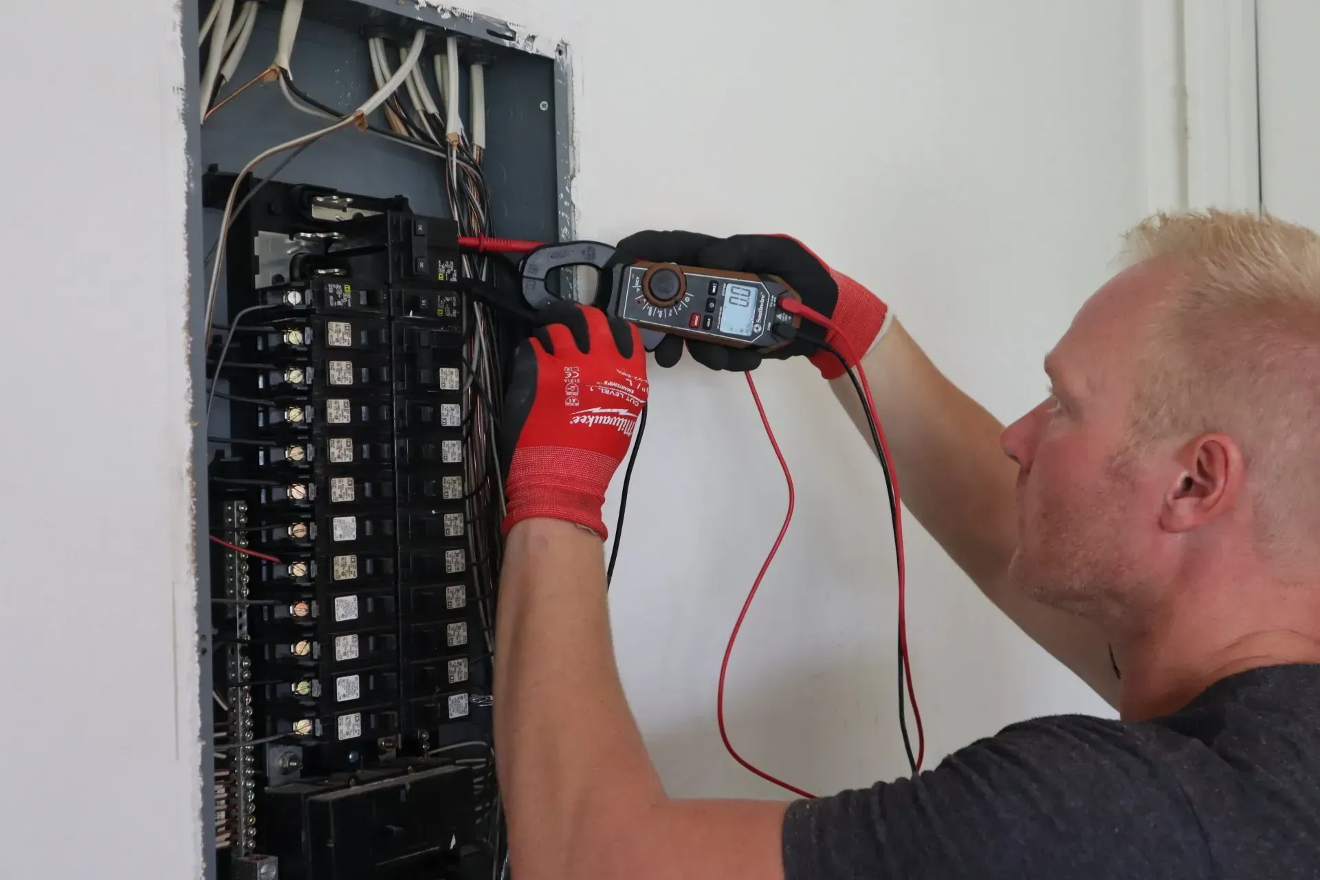 A man is working on an electrical panel with a clamp.