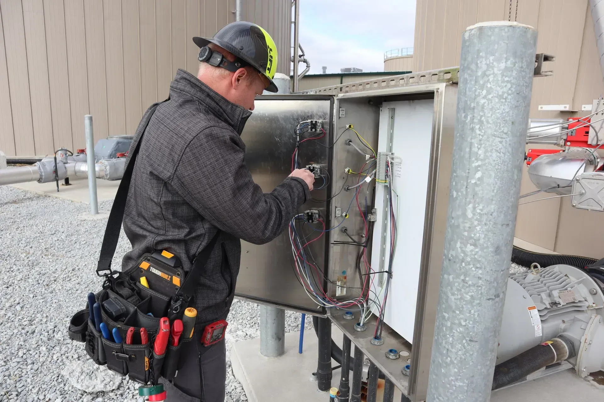 A man wearing a hard hat is working on an electrical box.