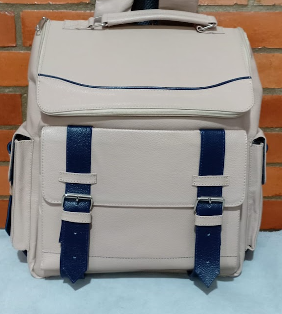 Mochila gris claro con correas azules contra una pared de ladrillos.