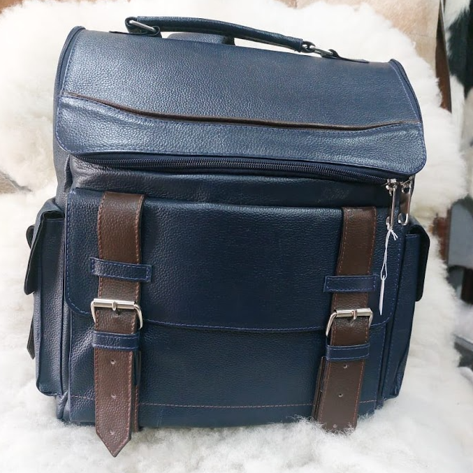 Bolso para cámara de piel azul oscuro con correas marrones sobre una superficie blanca y mullida.