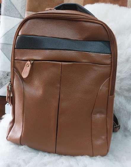 Mochila de cuero marrón con bolsillo frontal con cremallera y franja decorativa horizontal negra sobre una superficie clara.