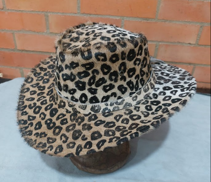 Sombrero de ala ancha con estampado de leopardo sobre un soporte apoyado contra una pared de ladrillos.